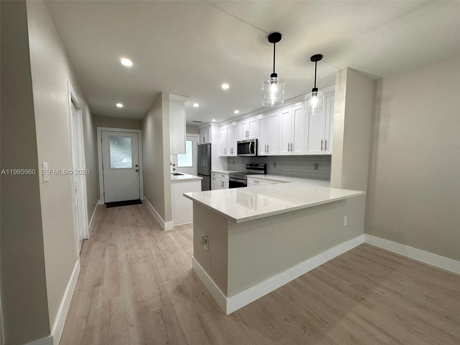 A kitchen features white cabinets, a quartz-topped island, and light wood-look flooring — 708 Victoria Dr # 101, Cape Coral FL 33904, CAPE CORAL, FL