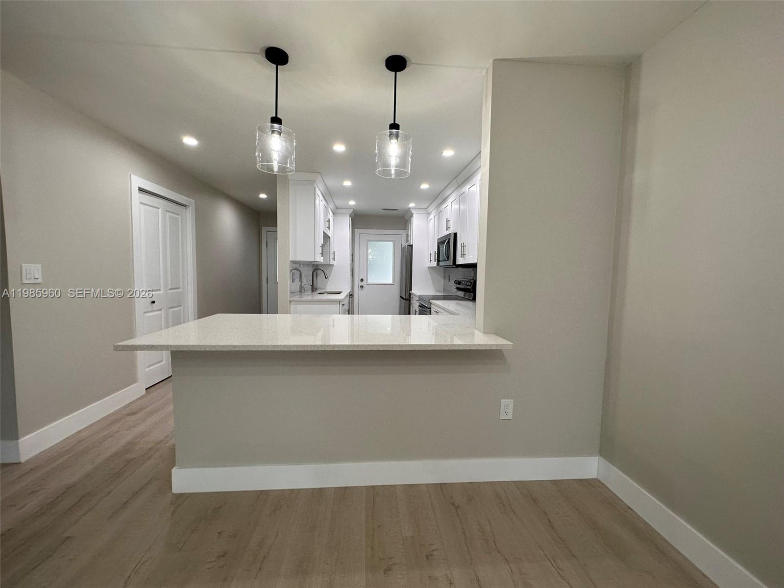 A kitchen features white cabinets, a quartz breakfast bar, and two glass pendant lights — 708 Victoria Dr # 101, Cape Coral FL 33904, CAPE CORAL, FL