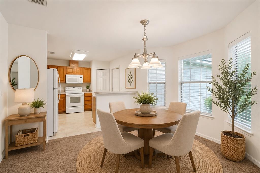 A dining area with a round wooden table, four chairs, and a kitchen in the background — 12104 NW 162ND DRIVE, ALACHUA, FL
