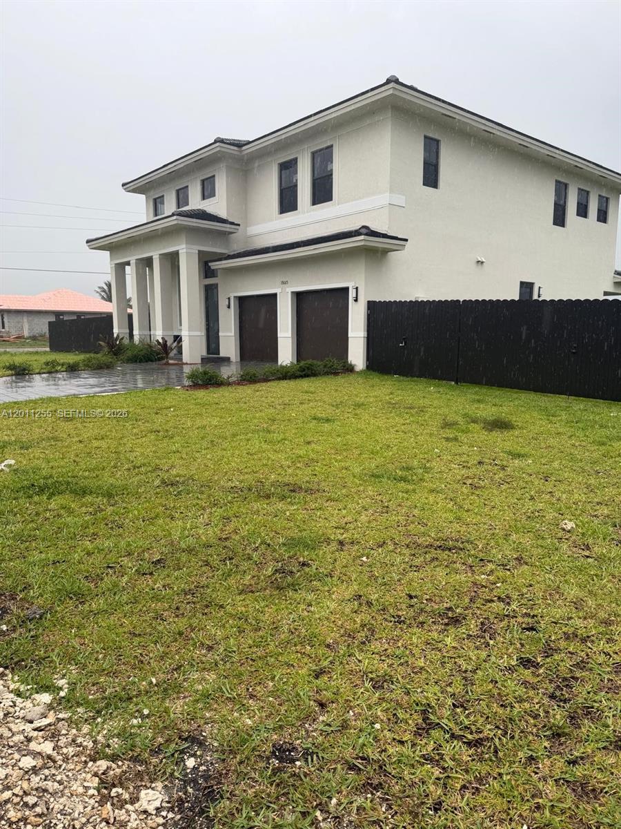 A two-story house with a light-colored exterior, dark garage doors, and a black fence — HOMESTEAD, FL