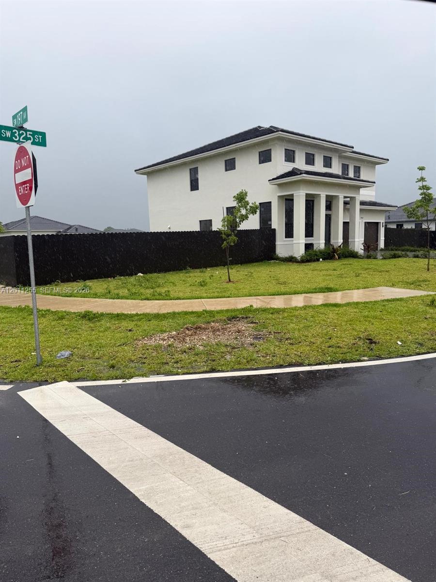A two-story white house stands behind a black fence at a street corner — HOMESTEAD, FL