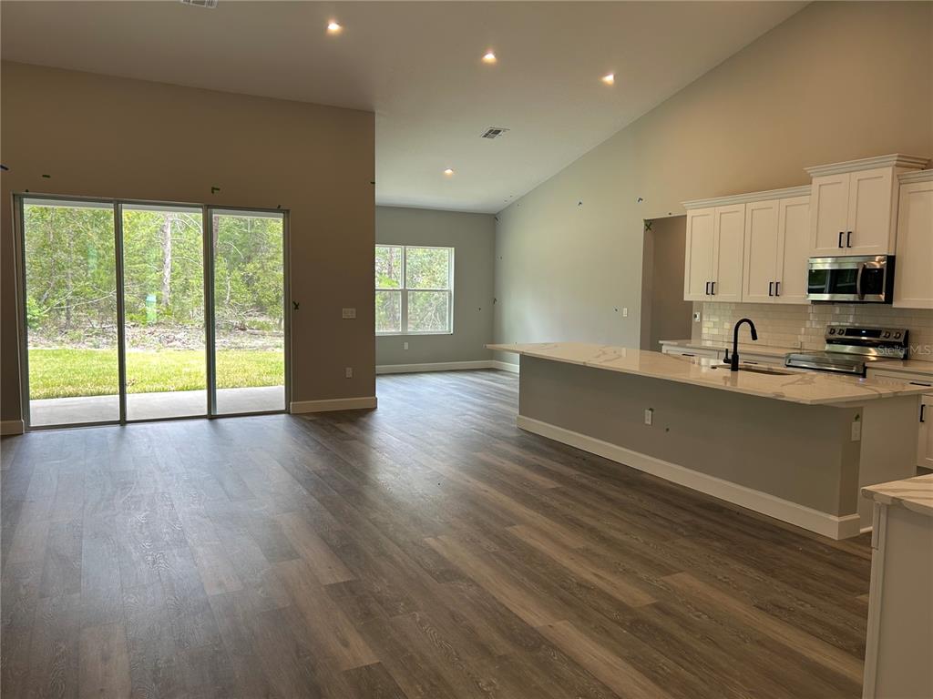 An open-concept kitchen and living area features light wood-look flooring, white cabinetry, and sliding doors — 3064 W PINE RIDGE BOULEVARD, BEVERLY HILLS, FL