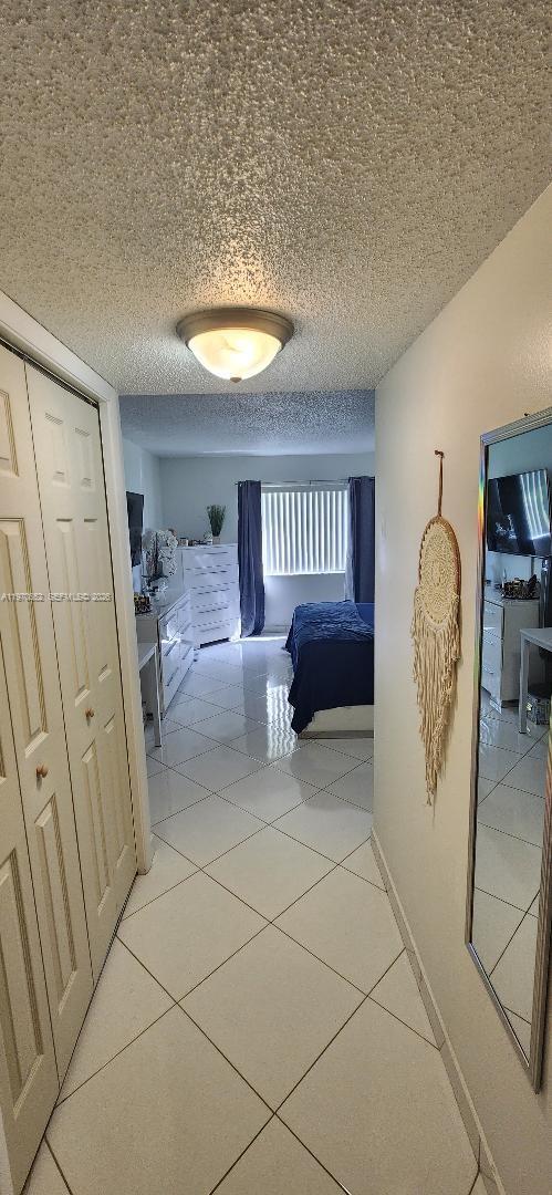 A hallway with white tile floors leads into a bedroom with a bed and dresser — 327 Lakeview Dr # 103, Weston FL 33326, WESTON, FL