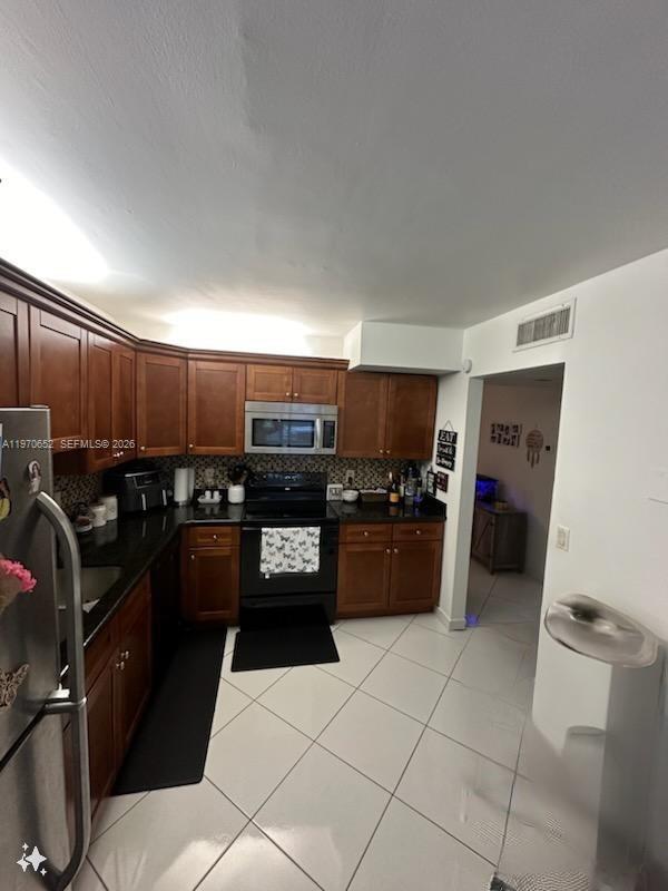 A kitchen features dark wood cabinets, black countertops, stainless steel appliances, and white tile flooring — 327 Lakeview Dr # 103, Weston FL 33326, WESTON, FL