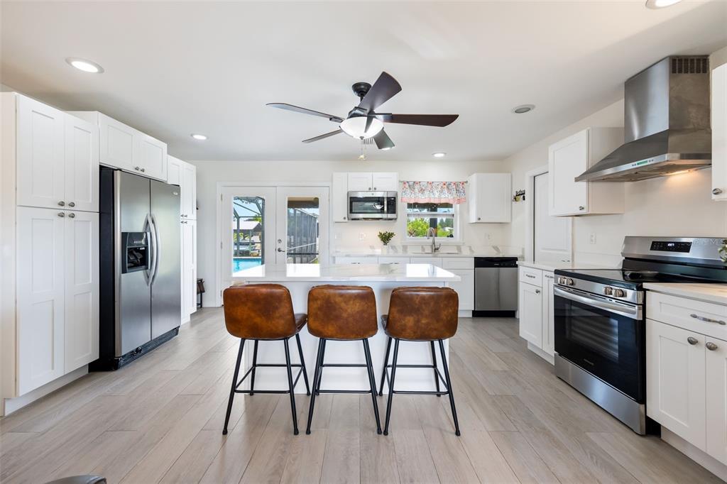 A modern kitchen features white cabinets, stainless steel appliances, a central island, and bar stools — 3601 WISTERIA PLACE, PUNTA GORDA, FL