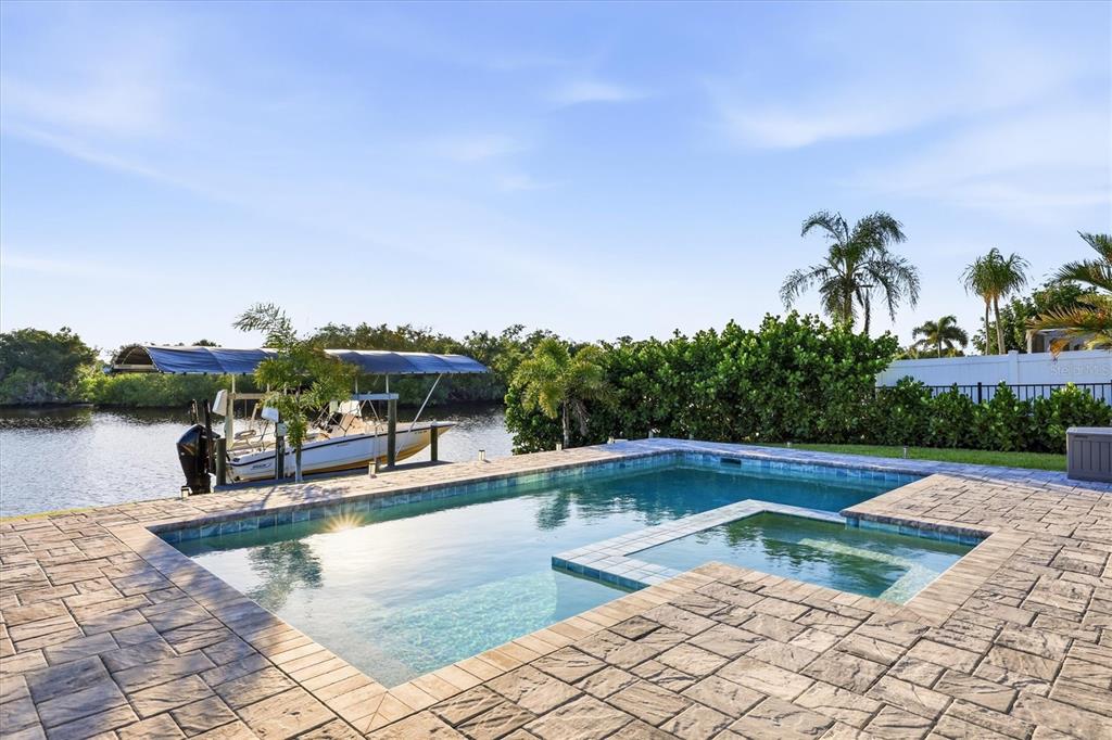 An outdoor swimming pool and spa overlook a canal with a boat on a lift — 430 SPRING LAKE BOULEVARD NW, PORT CHARLOTTE, FL
