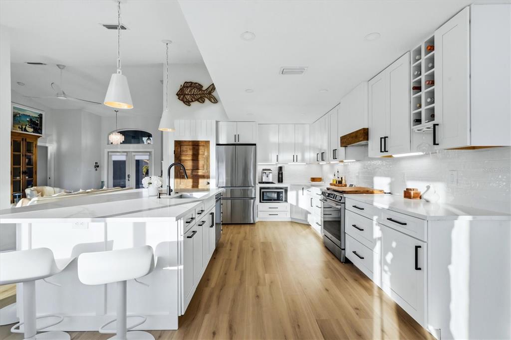 A bright, modern kitchen features white cabinetry, a large island, and light wood flooring — 430 SPRING LAKE BOULEVARD NW, PORT CHARLOTTE, FL