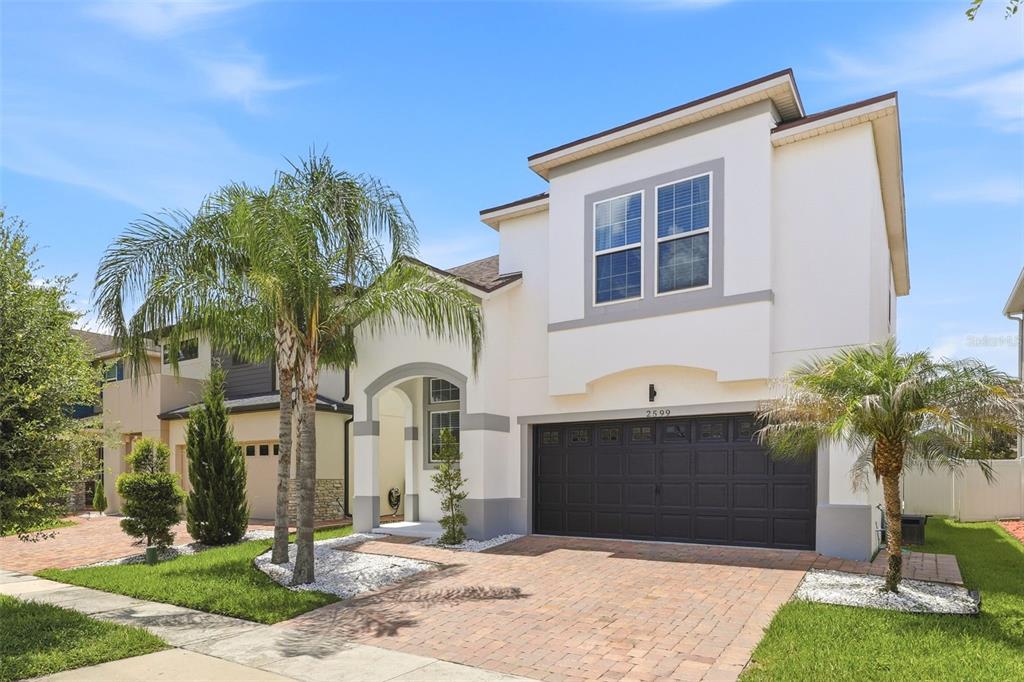 A two-story house with a white stucco exterior, a dark garage door, and palm trees — 2599 NOUVEAU WAY, KISSIMMEE, FL