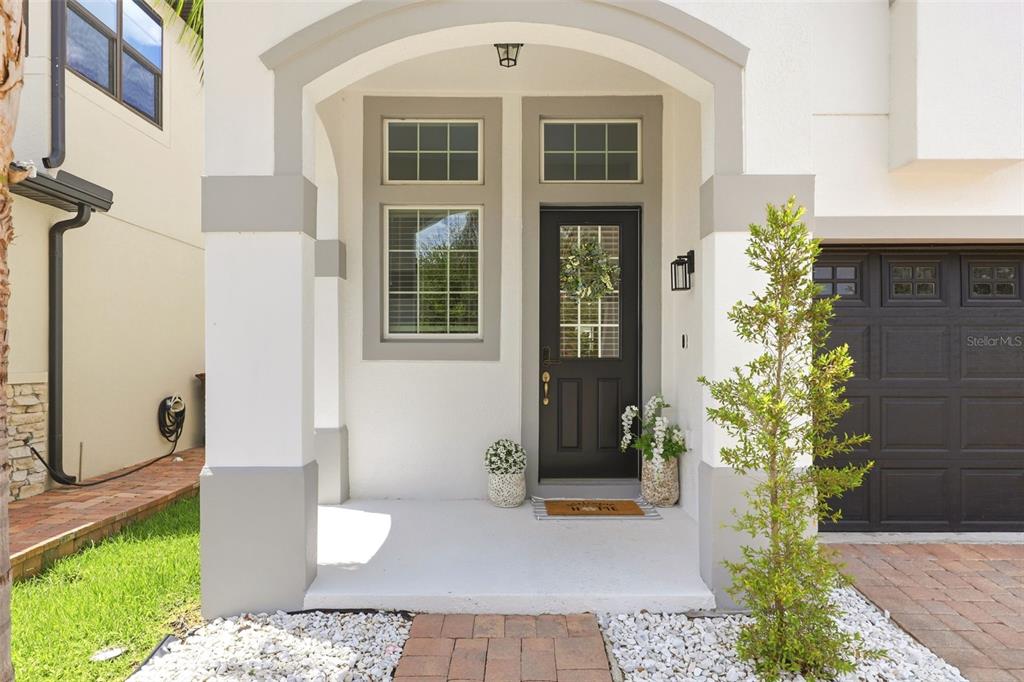 The exterior of a house features a covered entryway with a dark door and garage — 2599 NOUVEAU WAY, KISSIMMEE, FL