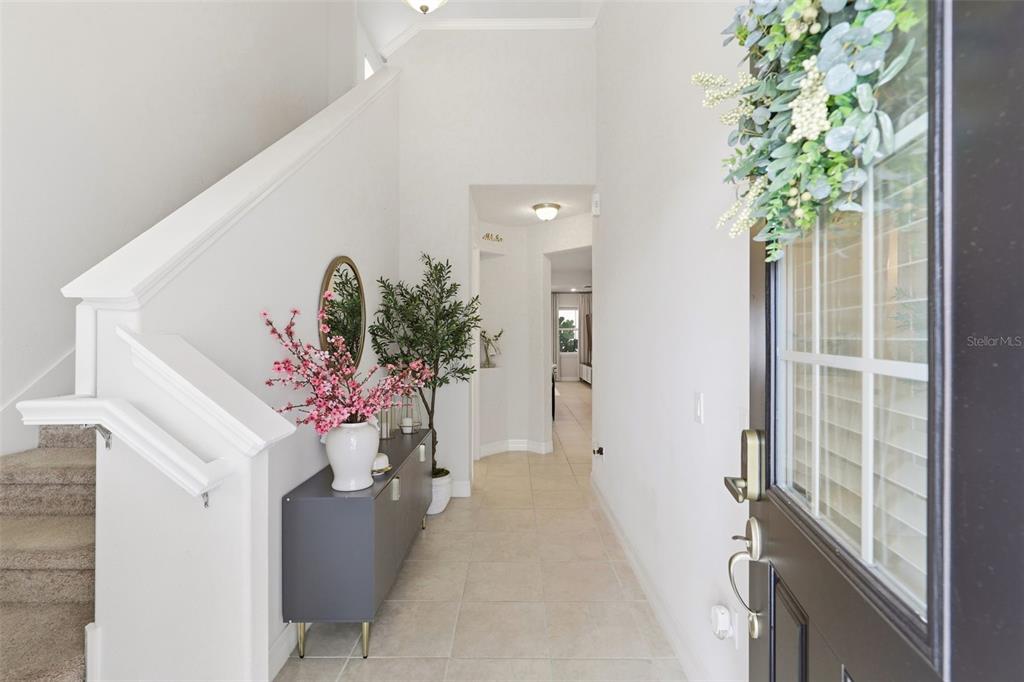 A bright entryway features a staircase, tile flooring, a console table, and a front door — 2599 NOUVEAU WAY, KISSIMMEE, FL
