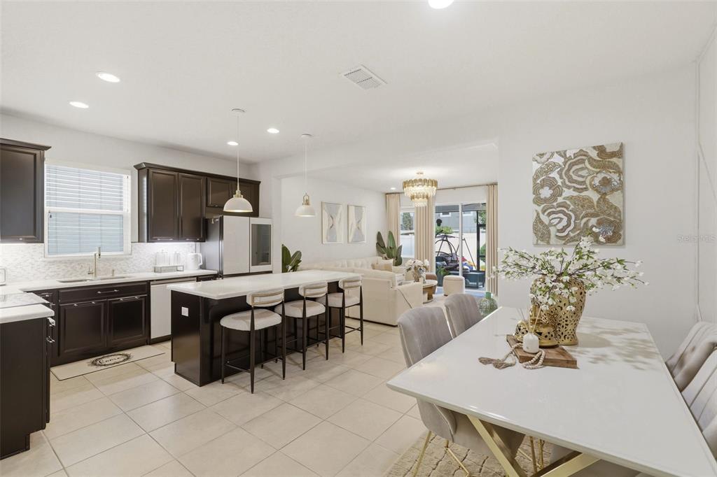A kitchen with dark cabinets and a white island opens into a dining and living area — 2599 NOUVEAU WAY, KISSIMMEE, FL