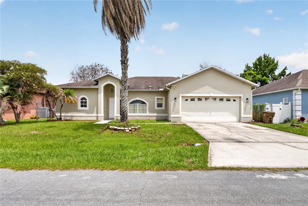 A single-story house with a beige stucco exterior, a two-car garage, and a palm tree — 121 AURELIA COURT, KISSIMMEE, FL