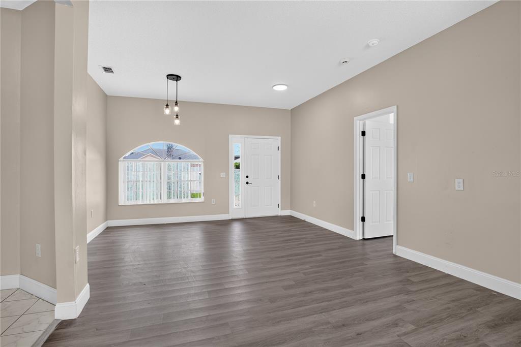 An empty room features gray wood-look flooring, beige walls, a white front door, and arched window — 121 AURELIA COURT, KISSIMMEE, FL
