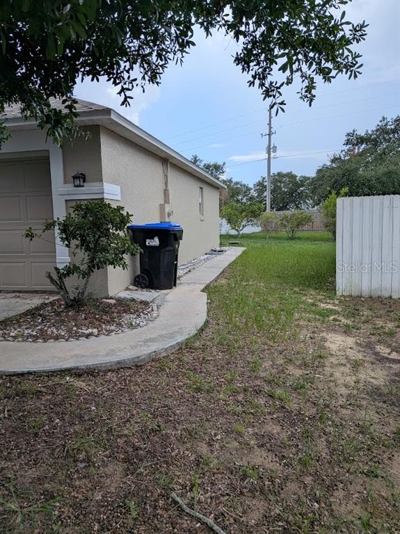 The side exterior of a house features a garage, a walkway, and a trash bin — 7885 CAMLYN COURT, ORLANDO, FL