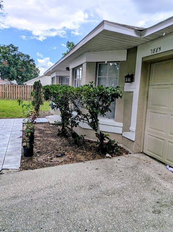 A tan house exterior features a garage, a small garden bed, and a paved walkway — 7885 CAMLYN COURT, ORLANDO, FL