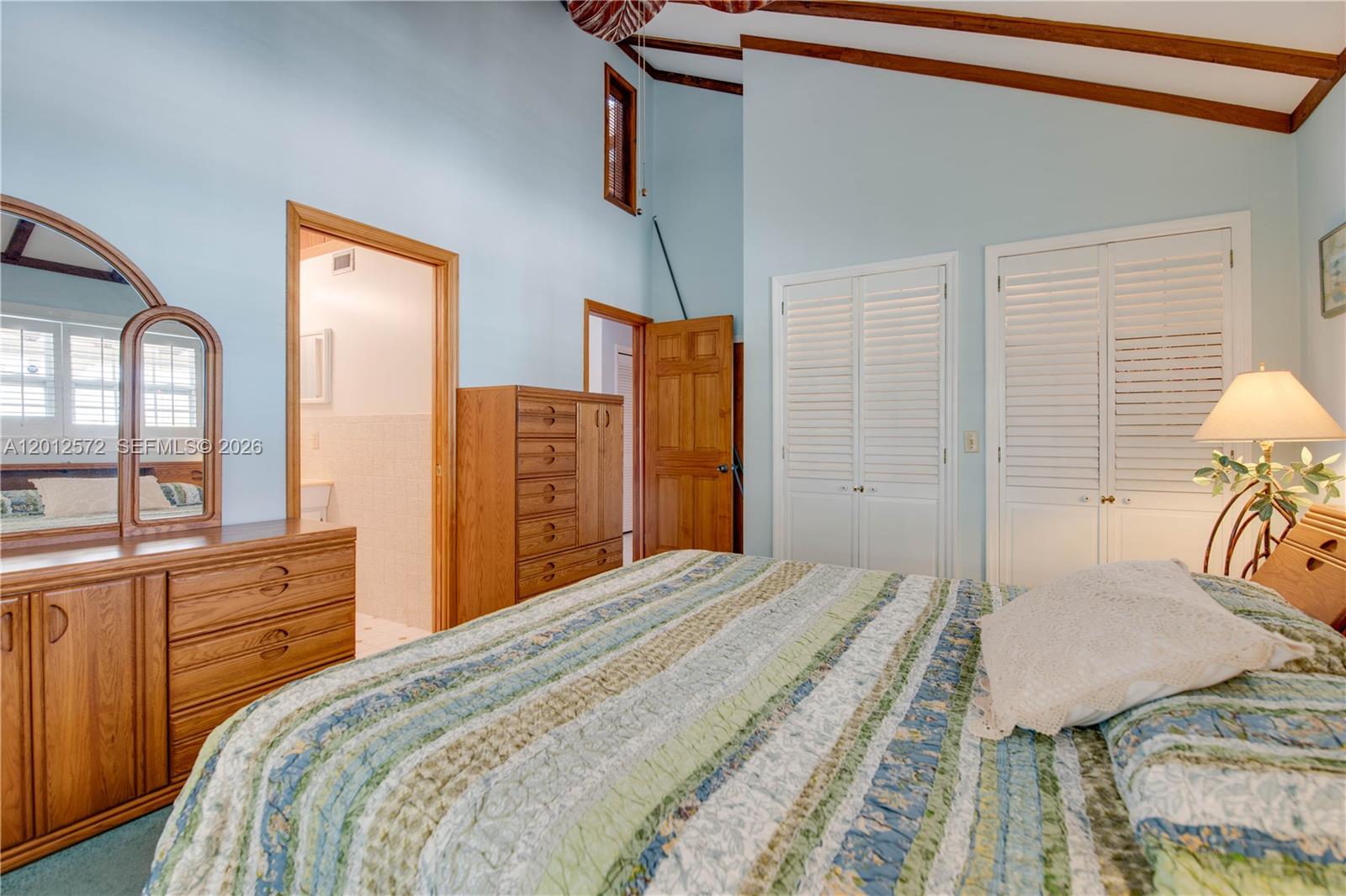 A bedroom features light blue walls, vaulted ceilings, wooden furniture, and two white louvered closets — 29662 Independence Ave, Big Pine FL 33043, BIG PINE, FL