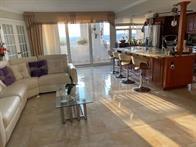 An open-concept living room features a white sectional sofa, glass coffee table, and kitchen island — 1340 S Ocean Boulevard # 1509, Pompano Beach FL 33062, POMPANO BEACH, FL