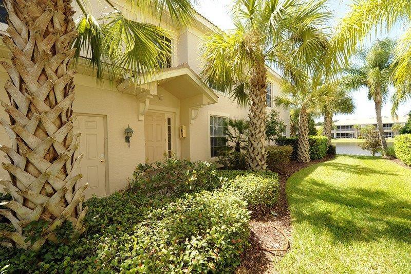 A beige two-story building exterior features a front entrance, palm trees, and landscaping — 7106 PROSPERITY CIRCLE UNIT 1201, SARASOTA, FL