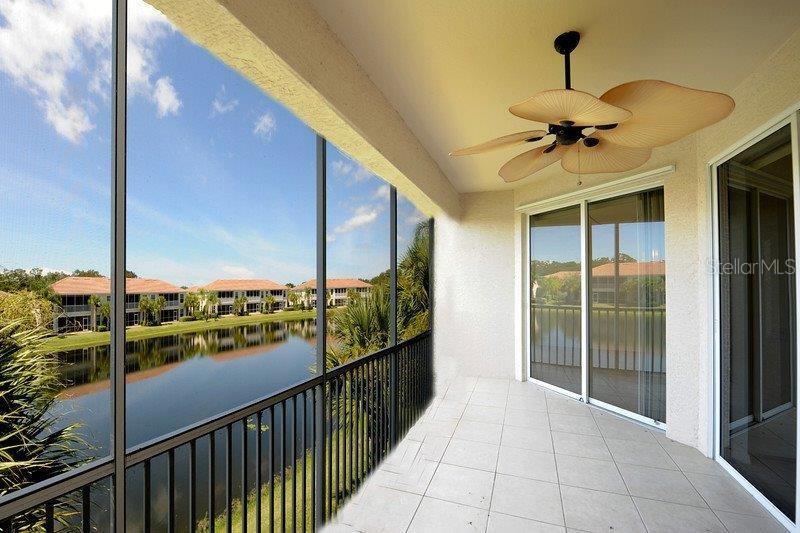 A screened-in balcony overlooks a lake and residential buildings, featuring a ceiling fan — 7106 PROSPERITY CIRCLE UNIT 1201, SARASOTA, FL