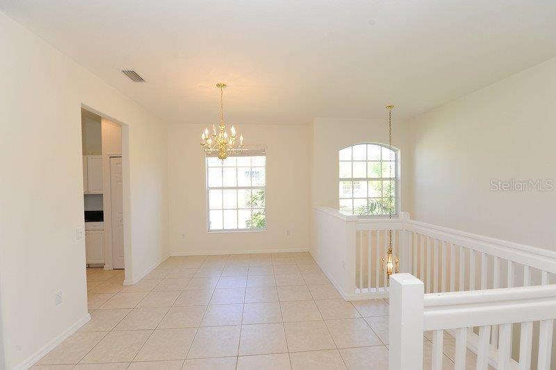 An interior view of a dining area with tile flooring, a chandelier, and a staircase railing — 7106 PROSPERITY CIRCLE UNIT 1201, SARASOTA, FL