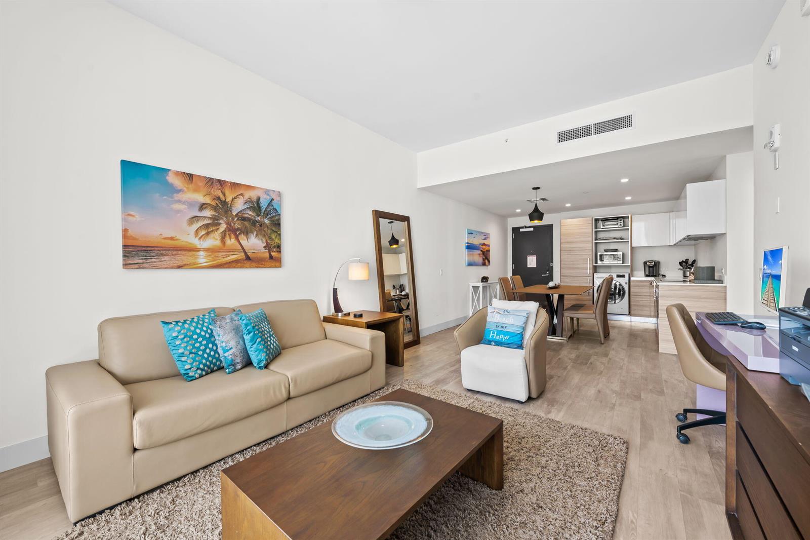 A living room with a beige sofa, coffee table, armchair, and an open-concept kitchen area — 777 N Ocean Drive # N407, Hollywood FL 33019, HOLLYWOOD, FL