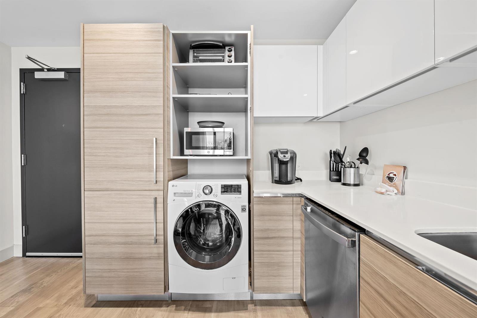 A modern kitchen features light wood cabinetry, white upper cabinets, a built-in washer, and appliances — 777 N Ocean Drive # N407, Hollywood FL 33019, HOLLYWOOD, FL