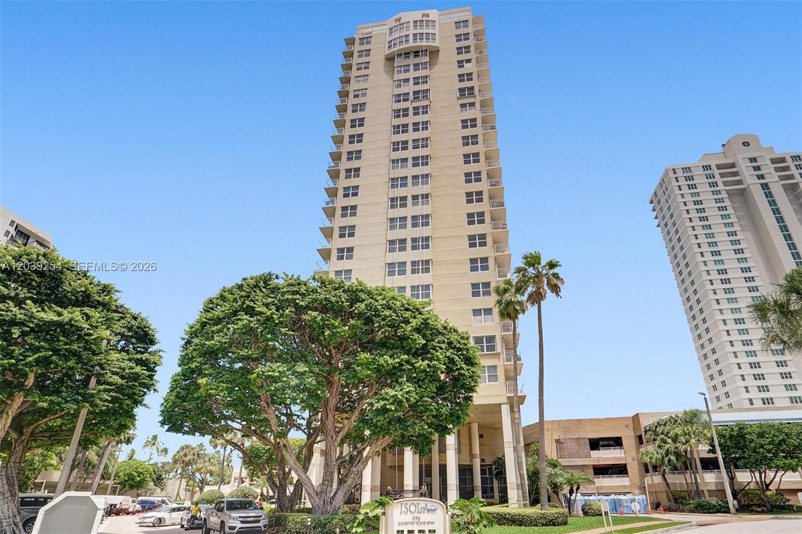 A tall residential high-rise building stands behind a large tree and a landscaped entrance sign — 770 Claughton Island Dr # 1014, Miami FL 33131, MIAMI, FL