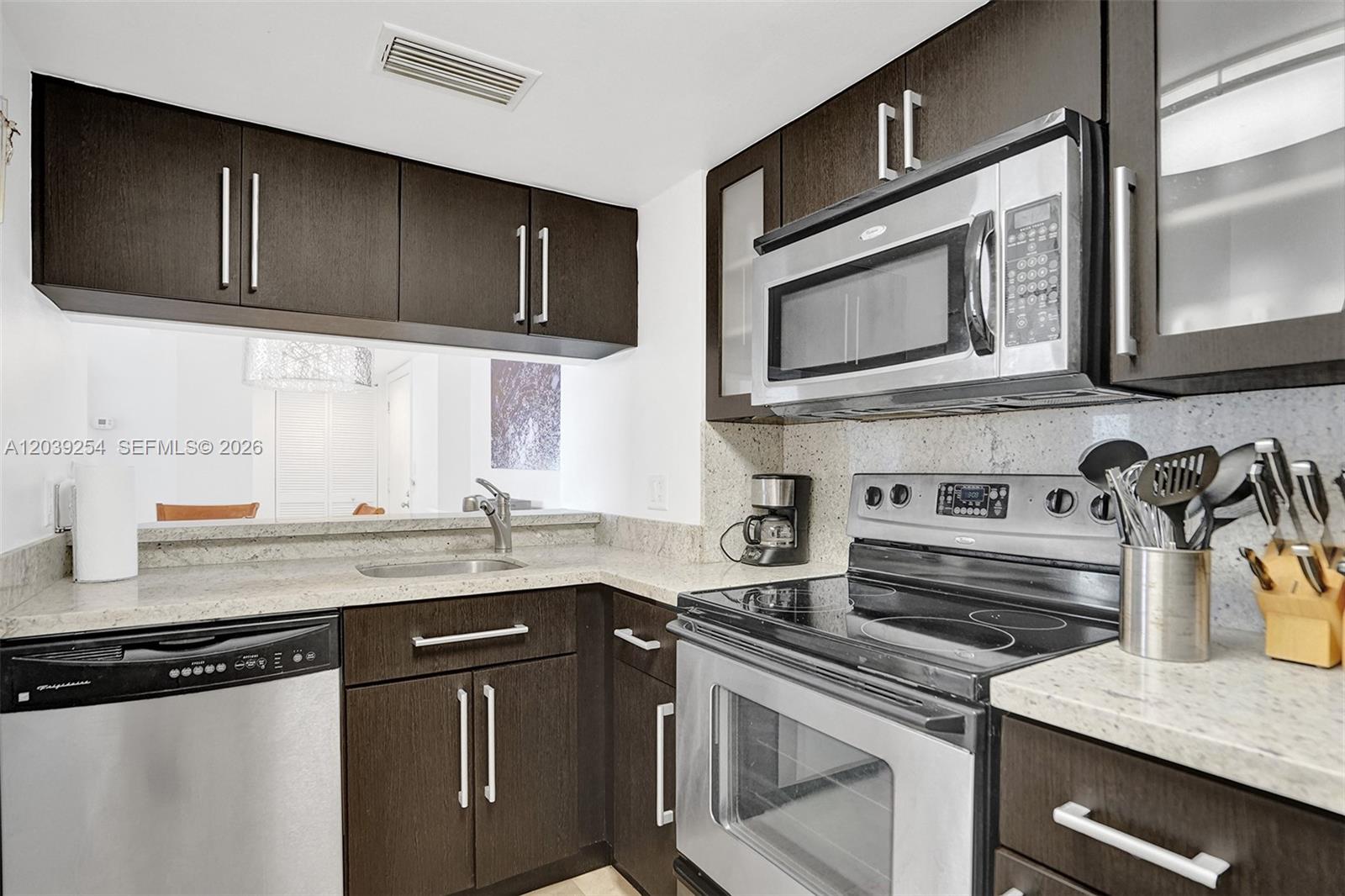 A kitchen features dark wood cabinets, stainless steel appliances, and light-colored granite countertops — 770 Claughton Island Dr # 1014, Miami FL 33131, MIAMI, FL