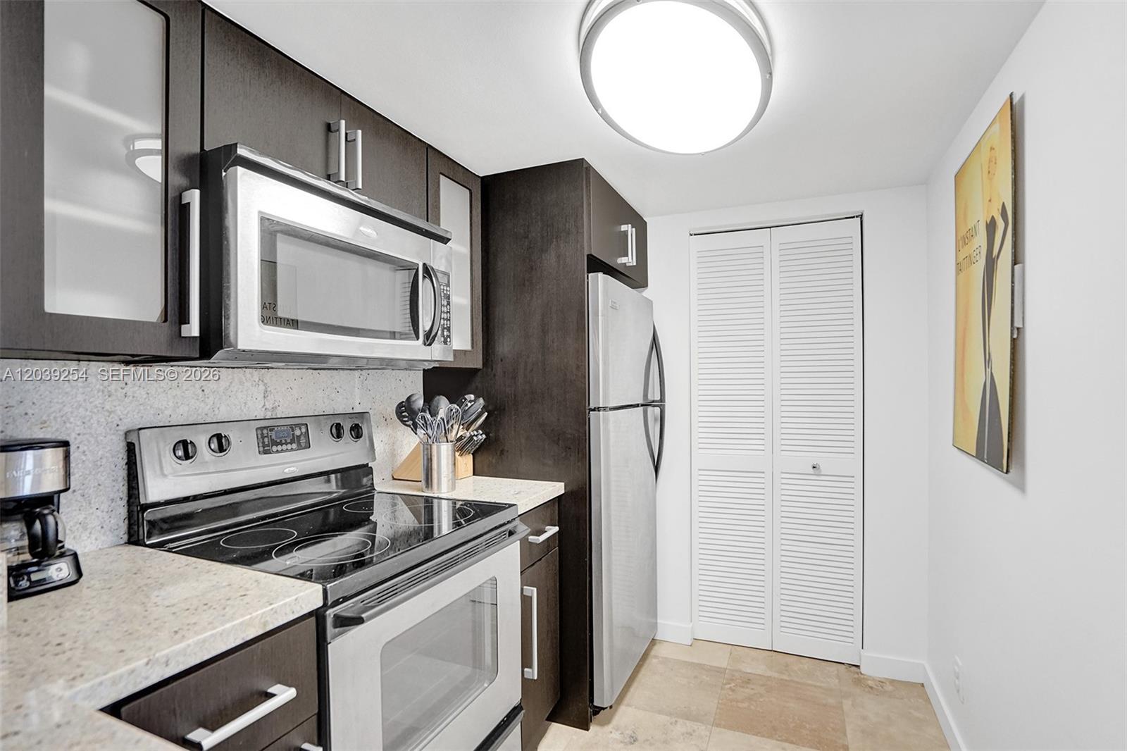 A galley kitchen features dark wood cabinets, stainless steel appliances, and light-colored stone countertops — 770 Claughton Island Dr # 1014, Miami FL 33131, MIAMI, FL