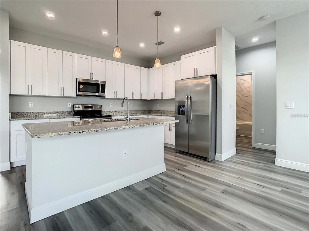 A modern kitchen features white cabinets, granite countertops, stainless steel appliances, and wood-look flooring — 15504 GREENWOOD AVENUE, PORT CHARLOTTE, FL