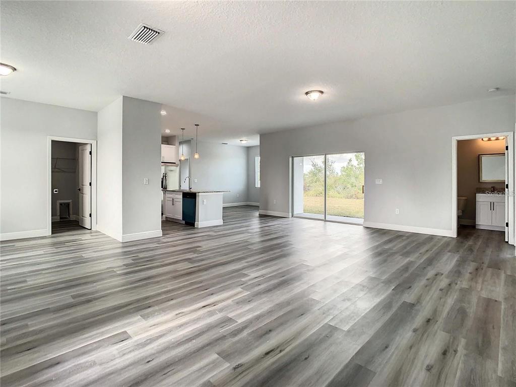 An open-concept living area with gray wood-look flooring, a kitchen island, and sliding glass doors — 15504 GREENWOOD AVENUE, PORT CHARLOTTE, FL