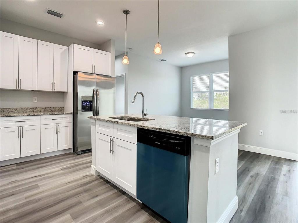 A kitchen features white cabinets, granite countertops, stainless steel appliances, and wood-look flooring — 15504 GREENWOOD AVENUE, PORT CHARLOTTE, FL
