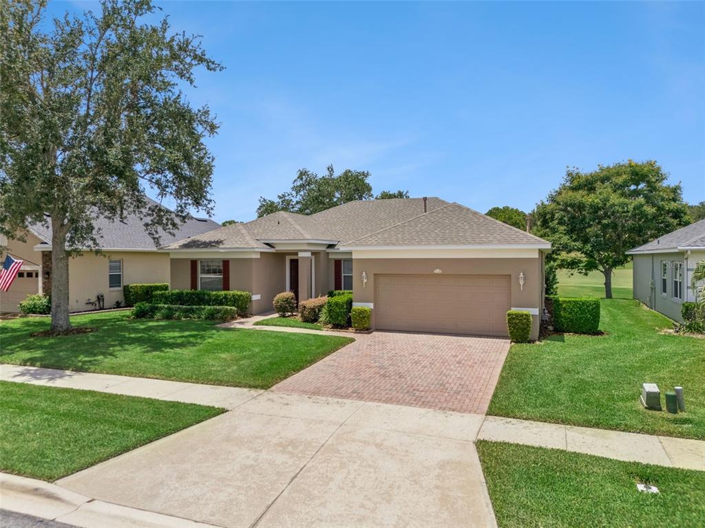 A single-story suburban house with a tan stucco exterior, a two-car garage, and a brick driveway — 1028 EVEREST STREET, CLERMONT, FL