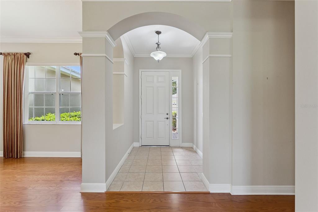 A tiled entryway features an arched opening, a white front door, and hardwood flooring nearby — 1028 EVEREST STREET, CLERMONT, FL