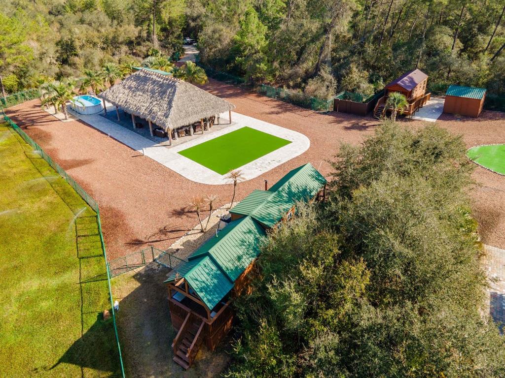 An aerial view shows a property with a thatched-roof pavilion, pool, and multiple wooden cabins — 5600 NE NFR 5, SILVER SPRINGS, FL