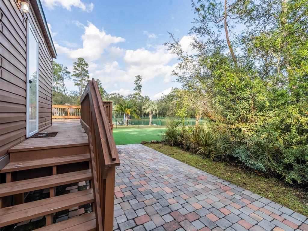 A wooden staircase leads to a deck overlooking a paved patio and a grassy yard — 5600 NE NFR 5, SILVER SPRINGS, FL