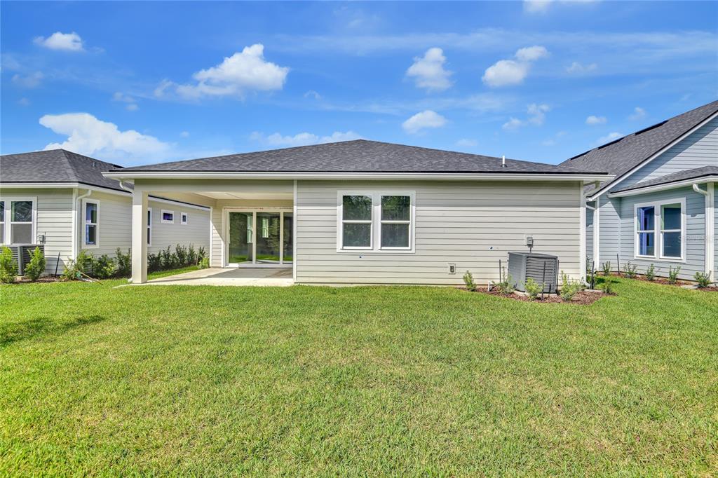 The rear exterior of a single-story house features light siding, a covered patio, and lawn — 219 THORNBERRY WAY, PALM COAST, FL