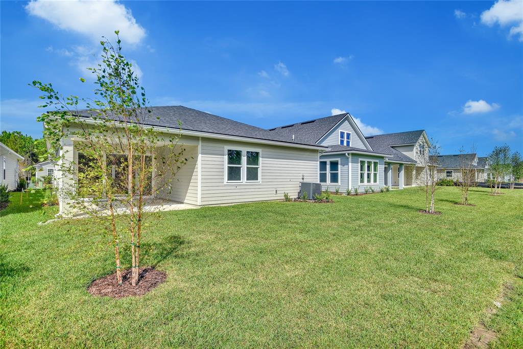 The exterior of a light-colored suburban house features a covered patio and a grassy yard — 219 THORNBERRY WAY, PALM COAST, FL