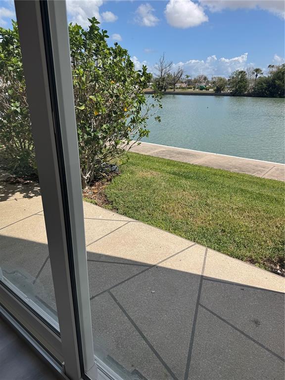 A view through a sliding glass door shows a patio, lawn, and a waterfront canal — 7425 BAY ISLAND DRIVE S UNIT 103, SOUTH PASADENA, FL