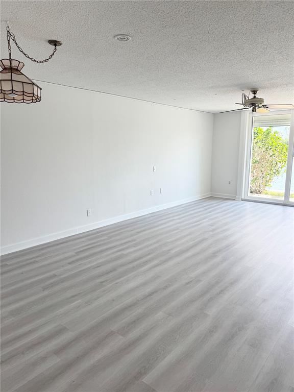 An empty room with light gray wood-look flooring, white walls, a ceiling fan, and sliding doors — 7425 BAY ISLAND DRIVE S UNIT 103, SOUTH PASADENA, FL
