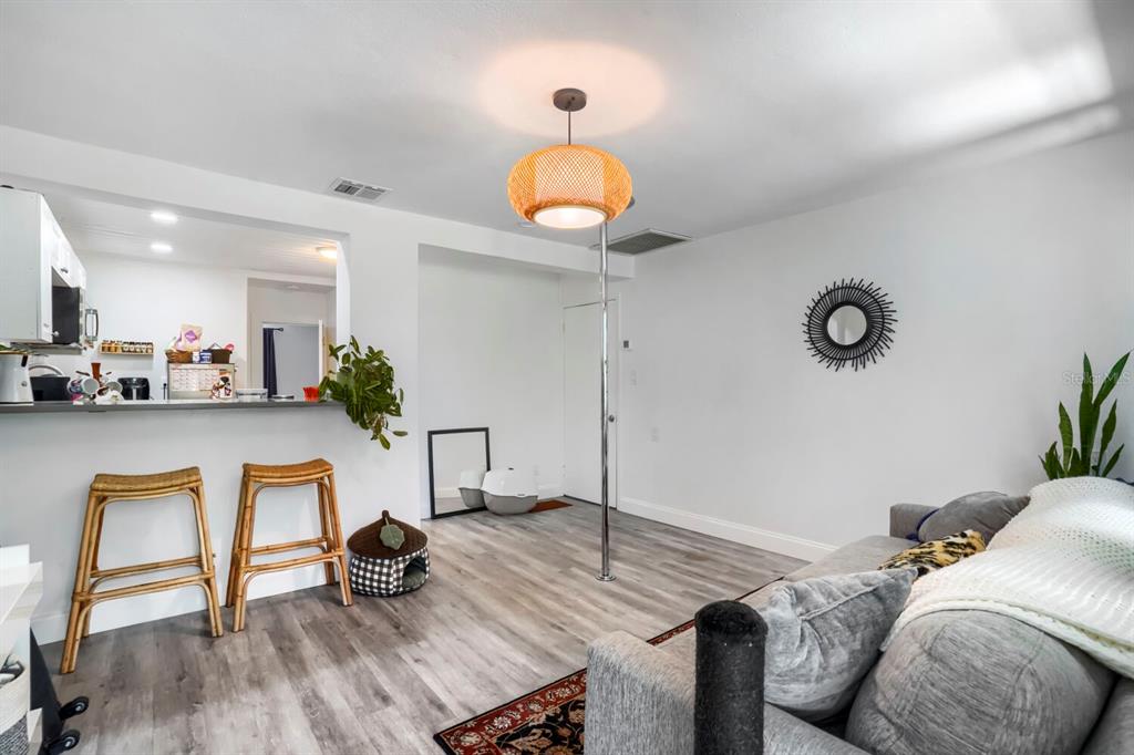 A living room with wood-look flooring, a kitchen pass-through, bar stools, and a dance pole — 940 25TH STREET N, ST PETERSBURG, FL
