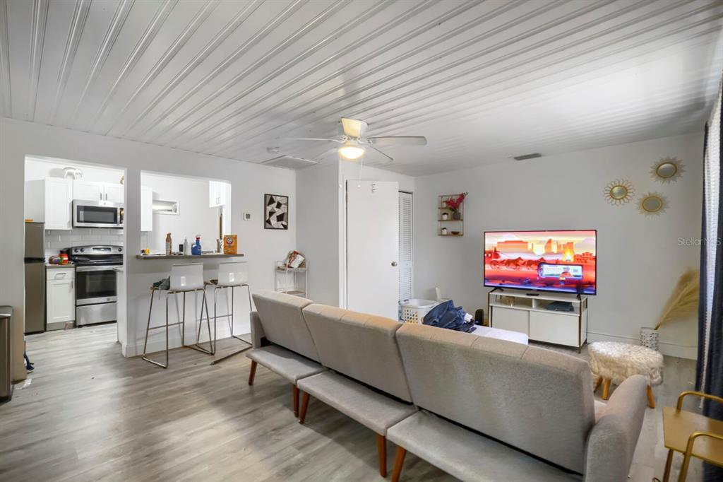 A living room with light wood-look flooring, a grey sofa, and a television on a stand — 940 25TH STREET N, ST PETERSBURG, FL