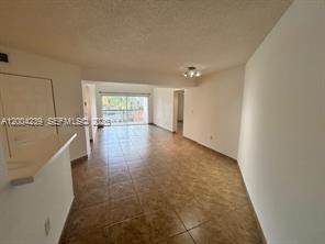An open-concept living area features tan tile flooring, white walls, and a sliding glass door — 6292 NW 186th St # 306, Hialeah FL 33015, HIALEAH, FL