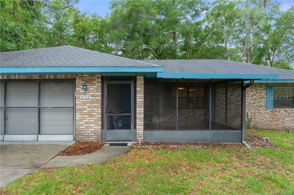 A single-story brick house features a screened-in front porch and a gray metal garage door — 3754 S APOPKA AVENUE, INVERNESS, FL
