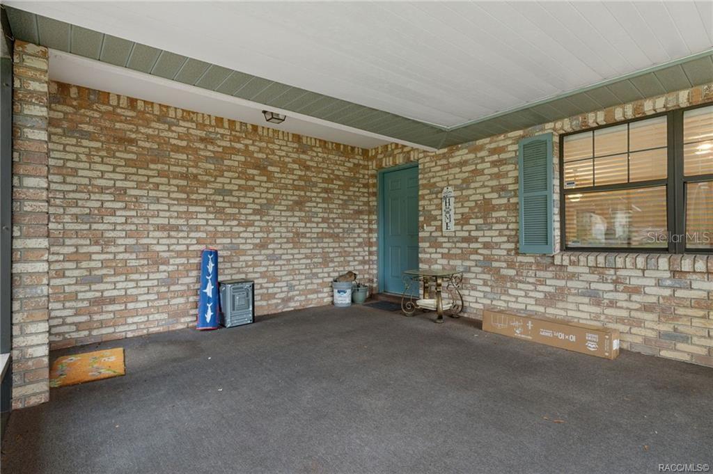 A covered brick porch features a teal front door, a window with shutters, and concrete flooring — 3754 S APOPKA AVENUE, INVERNESS, FL
