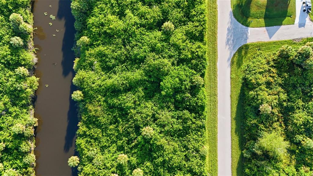 An aerial view shows a narrow canal bordering a dense wooded area and a road — 346 RUTLAND CIRCLE, PORT CHARLOTTE, FL