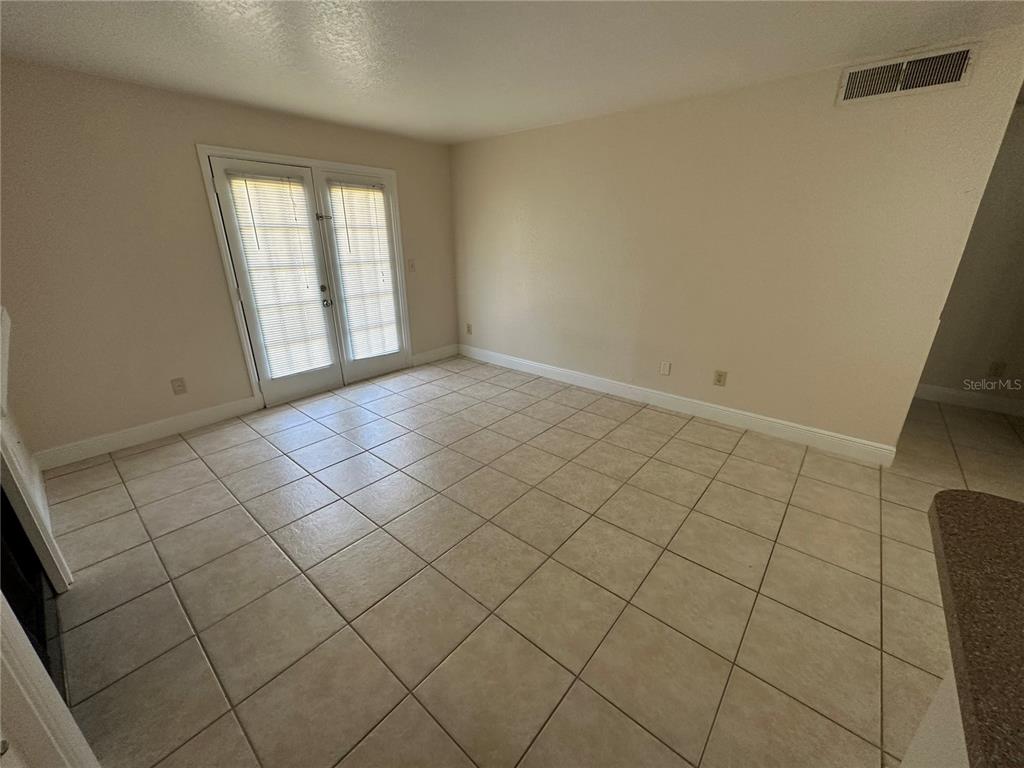 A room with beige tile flooring, light-colored walls, and a set of glass French doors — 2550 N ALAFAYA TRAIL UNIT 5103, ORLANDO, FL