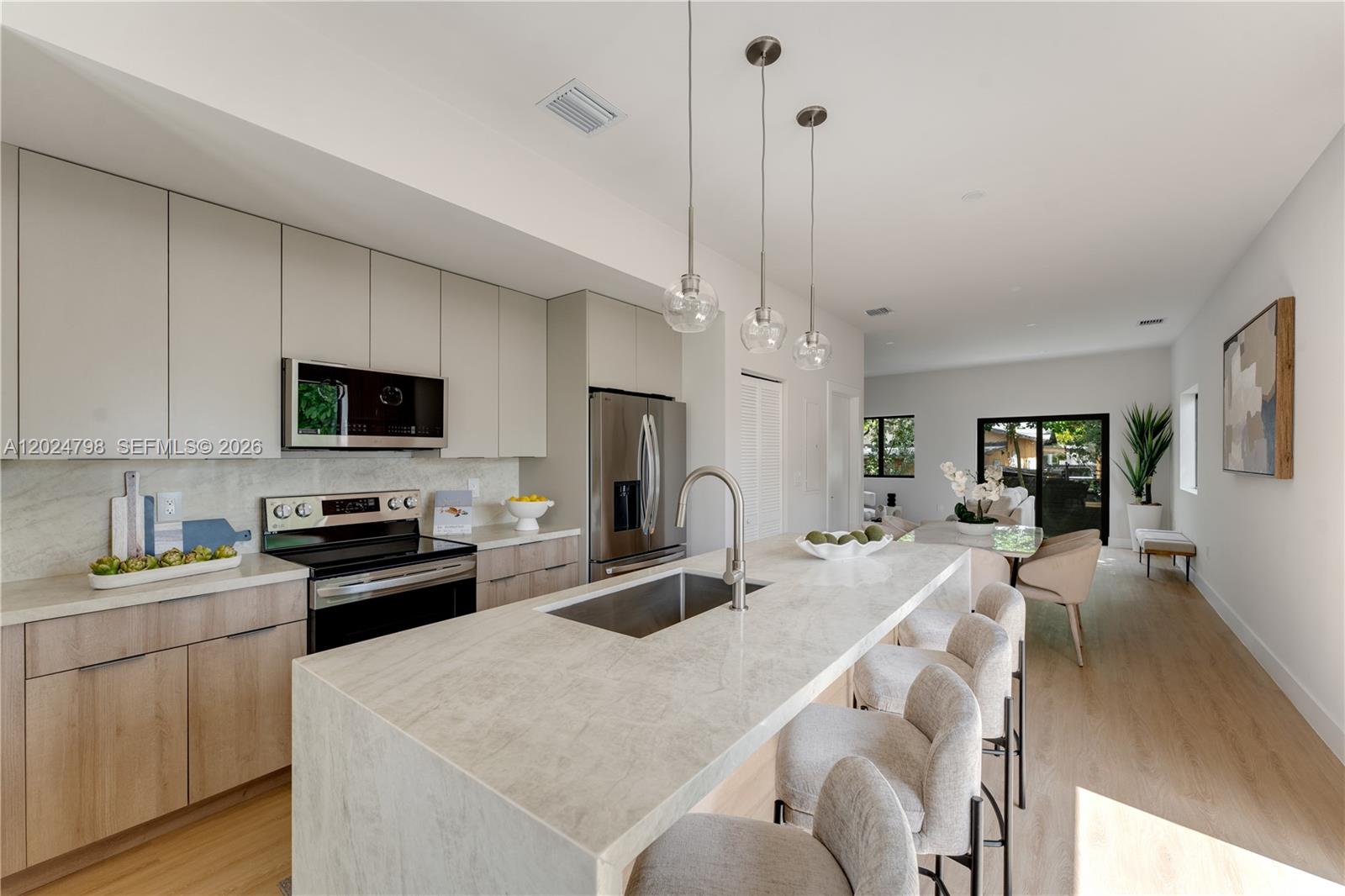 A modern kitchen features light wood cabinetry, a waterfall island with a sink, and pendant lighting — 1917 NW 17 ST # A, Miami FL 33125, MIAMI, FL