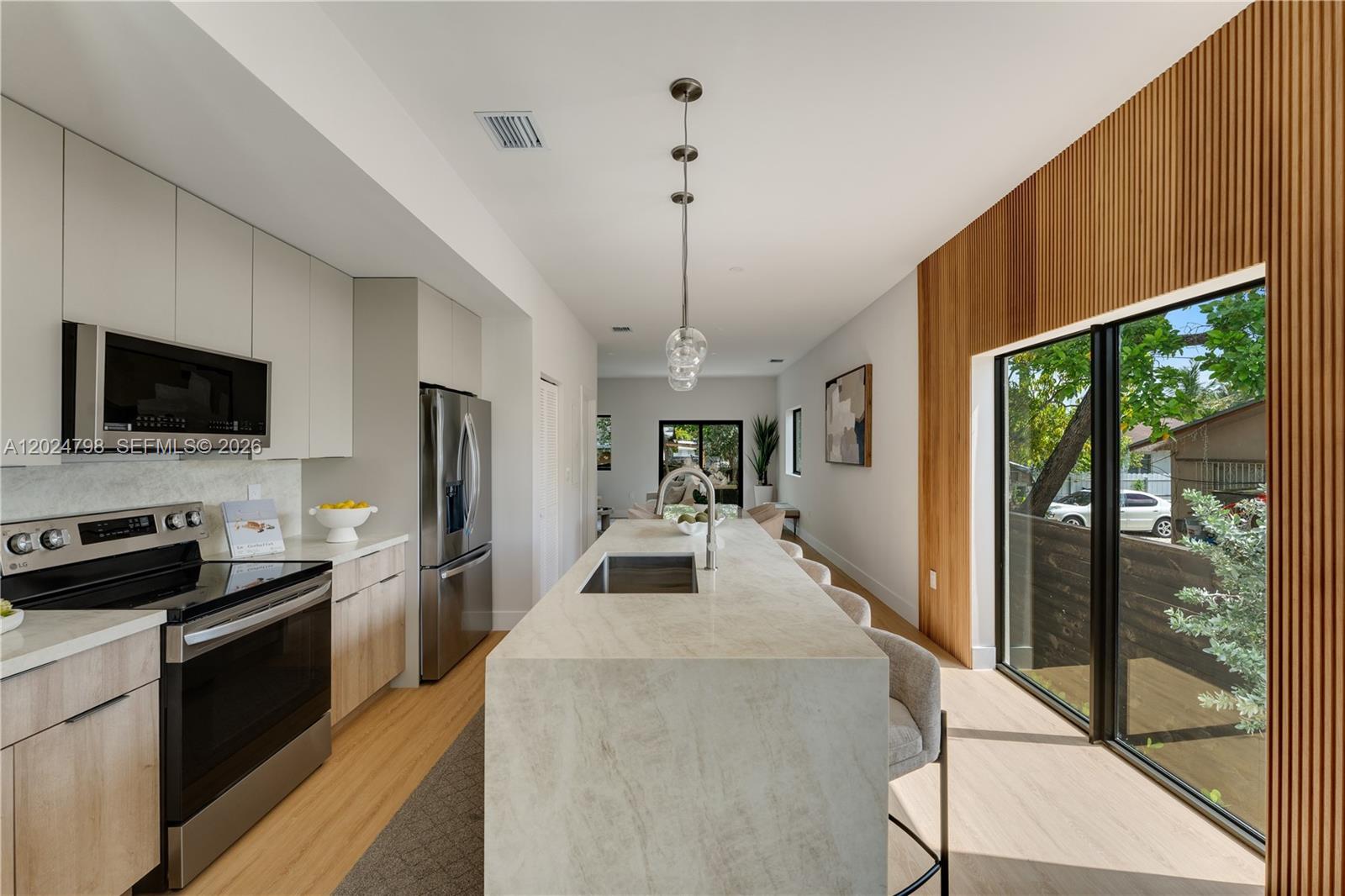 A modern kitchen features a stone island, light wood cabinetry, and a slatted wood accent wall — 1917 NW 17 ST # A, Miami FL 33125, MIAMI, FL