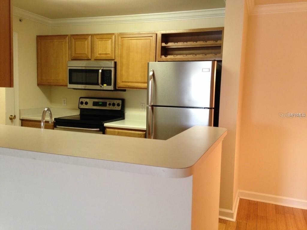 A kitchen features light wood cabinets, stainless steel appliances, and a white countertop breakfast bar — 18147 STERLING GATE CIRCLE UNIT 18147, TAMPA, FL